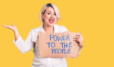 Genç sarışın ve cüsseli bir kadın gücü elinde tutuyor zaferi mutlu bir gülümsemeyle kutluyor ve ellerini kaldırarak kazanan bir ifade sergiliyor. 