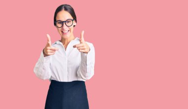 Profesyonel garson önlüğü giymiş güzel esmer bir kadın mutlu ve komik yüzüyle kamerayı işaret ediyor. iyi enerji ve titreşimler. 