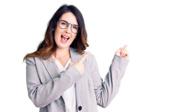 İş elbiseleri ve gözlük takan güzel esmer kadın gülümseyip kameraya bakıyor ve iki eliyle ve parmaklarıyla kenarı işaret ediyor.. 