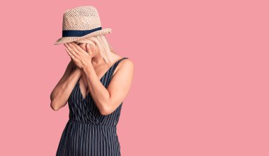 Yazlık şapka takan ve yüzünde üzgün bir ifade olan genç, güzel sarışın kadın ağlarken yüzünü elleriyle kapatıyor. depresyon kavramı. 