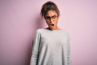Pembe arka planda süveter ve gözlük takan Afro-Amerikan genç ve güzel bir kız. Şok suratlı, şüpheci ve alaycı görünüyor.