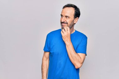 Orta yaşlı yakışıklı bir adam günlük tişört giyip izole edilmiş beyaz arka planda dikiliyor şüphe üzerine yoğunlaşıyor çenesinde bir parmak ile yukarı bakıyor ve merak ediyor.