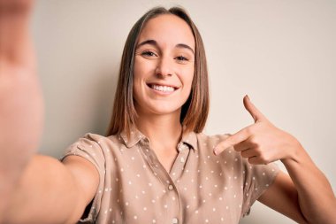 Yazlık tişört giyen genç bir kadın beyaz arka planda kamerayla selfie çekiyor. Yüzünde kendini gösteren sürpriz bir ifade var.