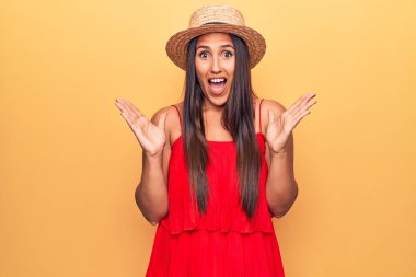 Genç, güzel esmer kadın yaz şapkası ve elbisesi ile zaferi kutluyor. Gülümsüyor ve ellerini kaldırarak kazanan yüz ifadesi takınıyor. 