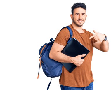 Sırt çantalı genç İspanyol adam elinde klasörle gülümsüyor. 