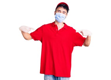 Teslimat üniforması giyen ve tıbbi maske takan genç İspanyol bir adam. Yüzünde gülümsemeyle kendinden emin görünüyor. Kendini gururlu ve mutlu bir şekilde gösteriyor.. 