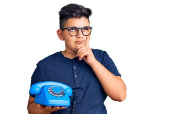 Küçük çocuk klasik telefon kullanıyor. Ciddi bir yüz. Soru sormayı düşünüyor. 