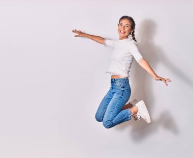 Saçları örgülü, sıradan kıyafetler giyen, mutlu gülümseyen genç ve güzel bir kadın. Yüzünde ve kollarında tebessümle atlayan izole beyaz arka planda açılan