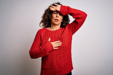 Orta yaşlı esmer kadın, günlük süveter giyip beyaz arka planda dikiliyor. Hastalık, ateş, grip ve virüs kapmak için alnına dokunuyor.