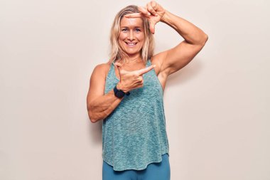 Orta yaşlı beyaz kadın spor kıyafetleri giyiyor gülümsüyor elleri ve parmakları mutlu yüzlü. yaratıcılık ve fotoğrafçılık kavramı. 