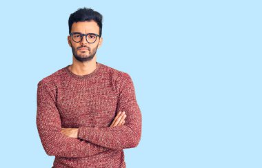 Kışlık süveter giyen, gözlüklü, kuşkucu ve gergin genç, yüzünde çapraz kollu tasvip etmeyen bir ifade. negatif kişi. 