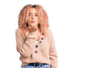 Kış kazağı giyen kıvırcık saçlı genç sarışın kadın kameraya bakıyor ve havada bir öpücük savuruyor. Güzel ve seksi. aşk ifadesi. 