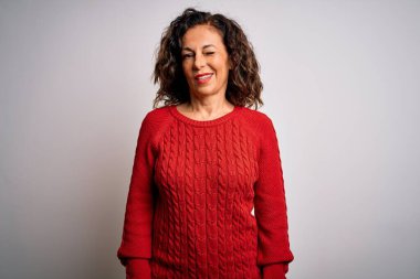 Orta yaşlı esmer kadın izole edilmiş beyaz arka planda dikilip kameraya seksi bir ifadeyle bakıyor, neşeli ve mutlu bir yüzle..