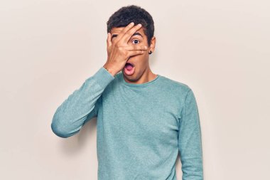 Genç Afrikalı Amerikalı sıradan kıyafetler giymiş. Şoka girmiş, yüzünü ve gözlerini eliyle kapatmış, parmaklarından korkuyla bakıyor. 