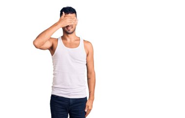 Gündelik kıyafetler giyen, gülümseyen ve gülümseyen genç İspanyol adam şaşırmak için gözlerini kapatıyor. kör kavram. 