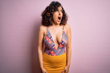 Genç, güzel bir Arap kadın, mayo ve güneş gözlüğü takıp pembe arka planda kızgın ve öfkeli çığlıklar atıyor. Öfkeyle bağırıyor. Öfke ve agresif kavram.