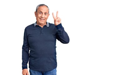 Kıdemli yakışıklı adam gündelik polo giyip iki numarayı gösterirken kendinden emin ve mutlu bir şekilde gülümsüyor.. 