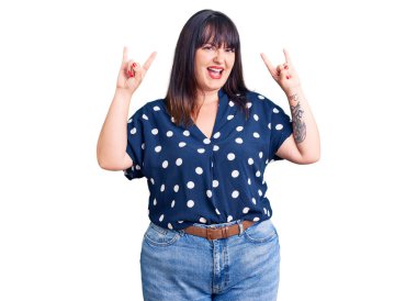 Genç ve cüsseli bir kadın gündelik kıyafetler giyip çılgın bir ifadeyle bağırıyor ve elleri havada rock sembolü yapıyor. Müzik yıldızı. ağır müzik konsepti. 