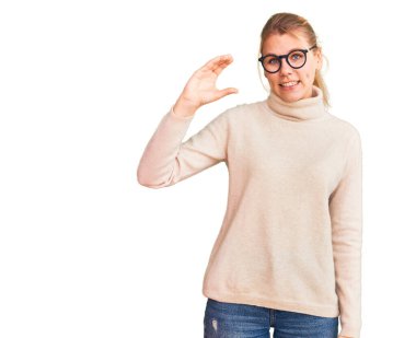 Balıkçı yaka kazak giyen, gözlüklü, gülümseyen, kendine güvenen, el hareketi yapan, parmaklarıyla işaret eden ve kameraya bakan güzel sarışın bir kadın. ölçüm kavramı. 