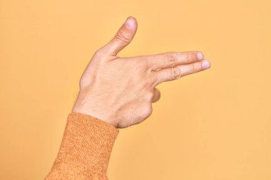 İzole edilmiş sarı arka planda parmaklarını gösteren beyaz bir gencin eli. Ateşli silahı parmaklarıyla işaret ediyor.