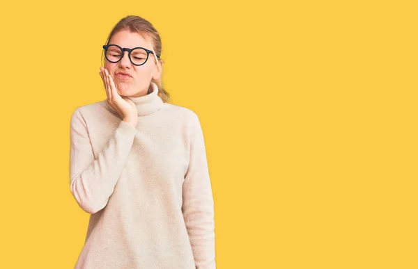아름다운 금발의 여자가 터틀넥 스웨터를 안경을 손으로 만지는 치통이나 병때문이다 — 스톡 사진