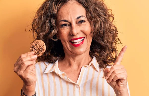 中世ブルネット女性保持Chocoletクッキー上の隔離された黄色の背景笑顔幸せなポインティングとともに手と指へザ側 — ストック写真