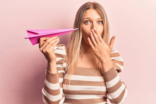 Молода Блондинка Тримає Паперовий Літак Покриваючи Рот Рукою Шокована Боїться — стокове фото