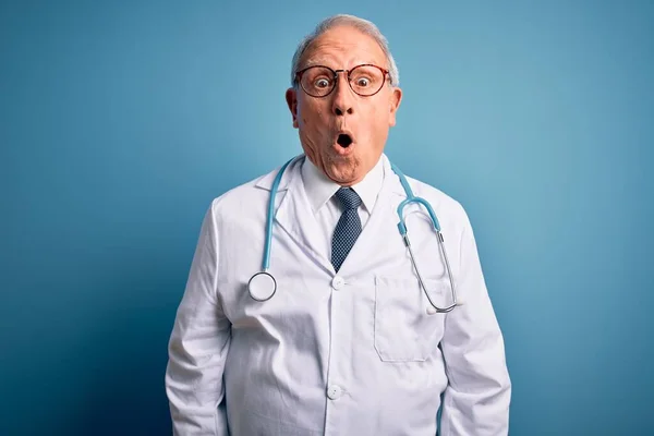 Starszy Siwowłosy Lekarz Noszący Stetoskop Płaszcz Medyczny Niebieskim Tle Przerażony — Zdjęcie stockowe
