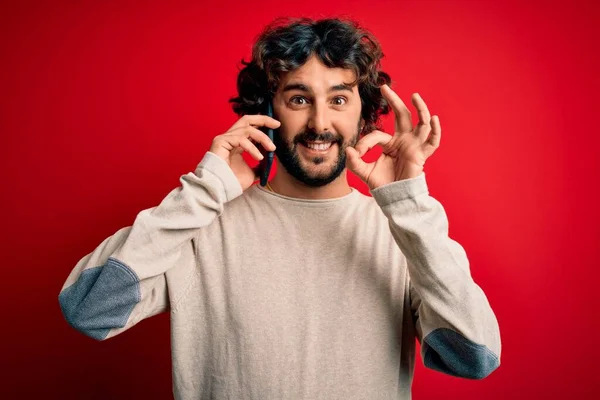 髭を生やしたハンサムな男が会話をしているスマートフォン上で話している赤い背景が指でOkサインをしている 優れたシンボル — ストック写真