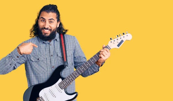 年轻的阿拉伯男子正在弹电吉他 手指对着一个人 面带微笑 兴高采烈 — 图库照片