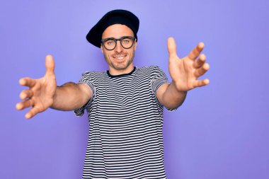 Mor arka plan üzerinde çizgili tişört ve Fransız beresi giyen yakışıklı bir adam sarılmak için kollarını açıp gülümseyen kameraya bakıyor. Mutluluğu kucaklayan neşeli bir ifade..