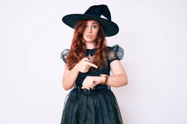 Cadıların cadılar bayramı kostümü giymiş genç ve güzel bir kadın. Aceleyle saati, sabırsızlığı ve gecikmeyi izlemek için işaret ediyor. 