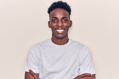 Sıradan kıyafetler giyen, kollarını kavuşturup kameraya gülümseyen Afro-Amerikan genç adam. pozitif kişi. 