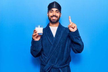 Uyku maskesi ve bornoz takan genç İspanyol bir adam bir fikir veya soruyla gülümseyen bir sütle gülümsüyor. 