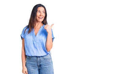 Genç, güzel, esmer, sıradan tişörtler giyen mutlu yüzüyle gülümseyen ve baş parmağıyla yüzünü gösteren bir kadın.. 