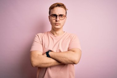 Genç, yakışıklı, günlük tişört giyen, pembe arka planda duran, kuşkucu ve gergin, kollarını kavuşturmuş, tasvip etmeyen bir yüz ifadesi takınan bir adam. Negatif kişi.