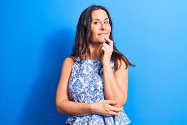 Mavi arka planda kolsuz tişört giyen genç, güzel esmer kadın kameraya kolları çapraz ve çenesi açık gülümsüyor. Olumlu düşünüyorum..