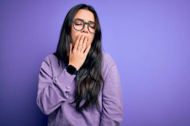 Mor izole arka planda gözlük takan genç esmer kadın ağzıyla ağzını kapatmaktan sıkılmış. Huzursuz ve uykulu..