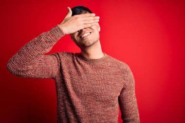 Kırmızı arka planda inek gözlüğü takan genç, yakışıklı İspanyol bir adam. Gülümsüyor ve yüzünde şaşkınlıktan gözleri kapayarak gülüyor. Kör kavram.