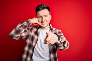 Kırmızı izole edilmiş arka plan üzerine gündelik modern tişört giyen yakışıklı beyaz bir adam gülümsüyor telefonda konuşuyor ve seni işaret ediyor. Ara beni..