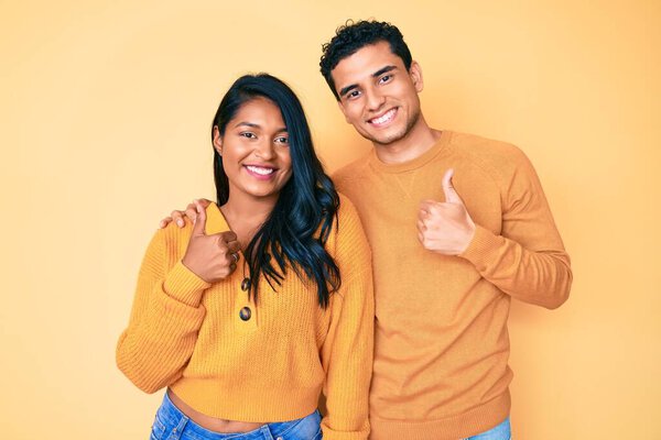 Beautiful latin young couple wearing casual clothes together success sign doing positive gesture with hand, thumbs up smiling and happy. cheerful expression and winner gesture. 