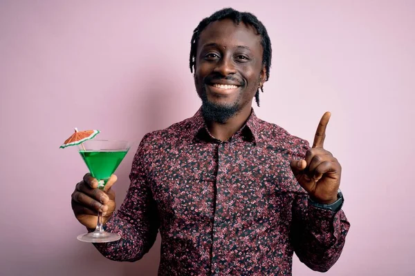 Young african american man drinking green cocktail. beverage over pink background surprised with an idea or question pointing finger with happy face, number one