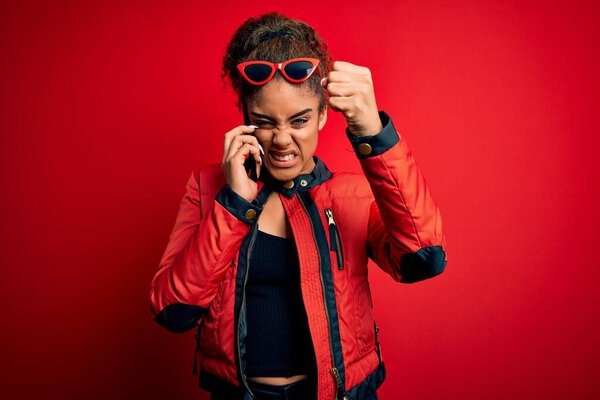 Молодая африканская американская девушка разговаривает по смартфону на красном фоне раздраженный и разочарованный кричать от гнева, сумасшедший и кричать с поднятой рукой, гнев концепции