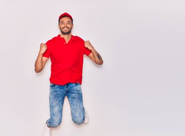 Mutlu gülümseyen üniformalı yakışıklı İspanyol teslimatçı. Yüzünde tebessümle zıplıyor, beyaz arka planda yumruklar havada kutluyor..