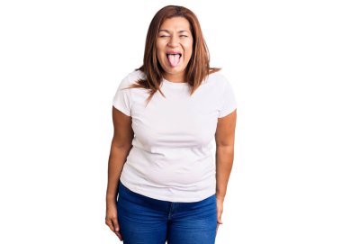 Orta yaşlı, beyaz tişört giyen Latin bir kadın komik bir ifadeyle dilini dışarı çıkartıyor. duygu kavramı. 