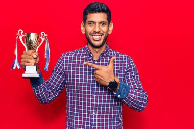 Elinde kupa tutan genç latin adam gülümsüyor mutlu el ve parmaklarıyla işaret ederek 