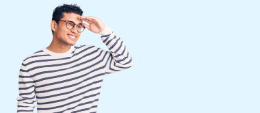 İspanyol yakışıklı genç adam gündelik kıyafetler ve gözlük takıyor çok mutlu ve tebessüm ediyor. arama kavramı. 