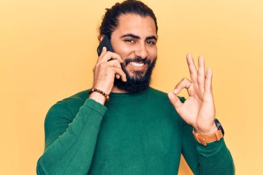 Genç Arap adam akıllı telefondan konuşuyor parmaklarıyla imza atıyor, gülümsüyor ve mükemmel bir sembol oluşturuyor. 