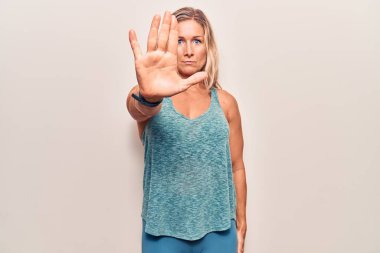 Orta yaşlı beyaz kadın spor giysisi giyiyor. Avuç içiyle şarkı söylemeyi kesiyor. Yüzünde olumsuz ve ciddi bir jest olan uyarı ifadesi. 