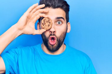 Sakallı, elinde çikolatalı kurabiye olan yakışıklı bir genç. Korkmuş ve ağzı açık bir şekilde şaşırmış. Şaşırmış ve şaşırmış. 